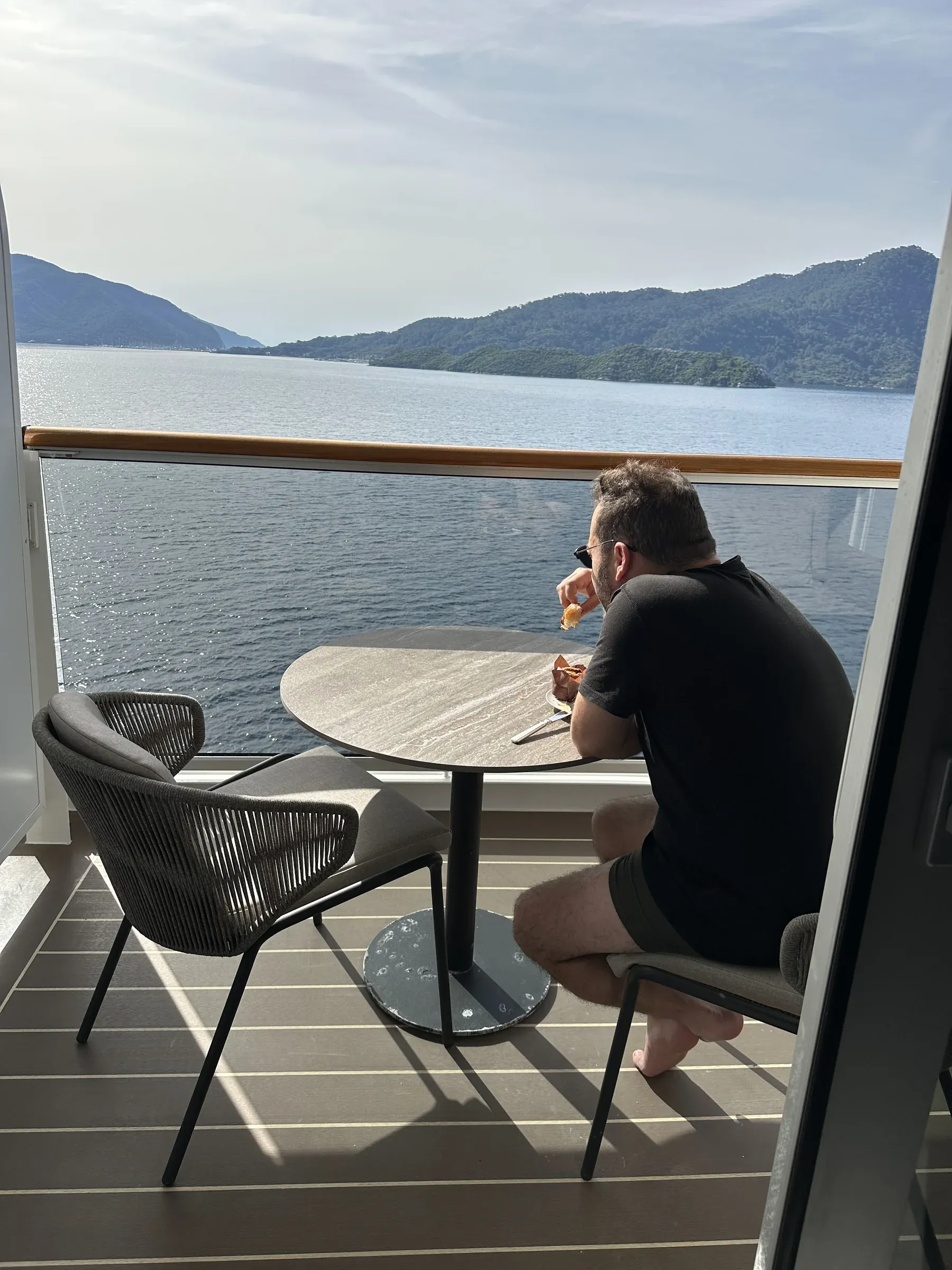 Me at a table on my suite's private terrace aboard Explora I, the Mediterranean coast beyond the rail