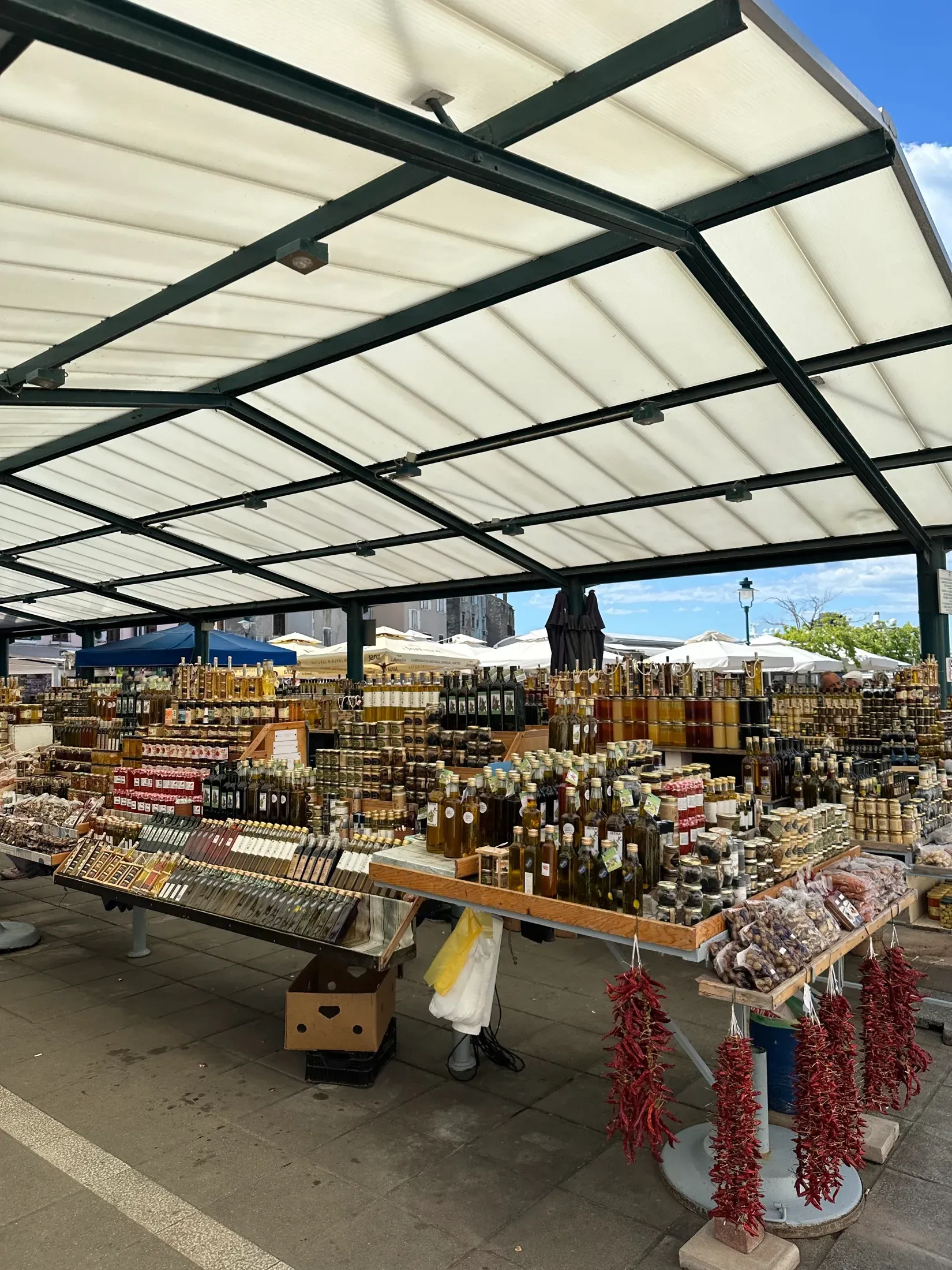 An open-air market stall of olive oil, honey, and dried chillies in a Mediterranean port