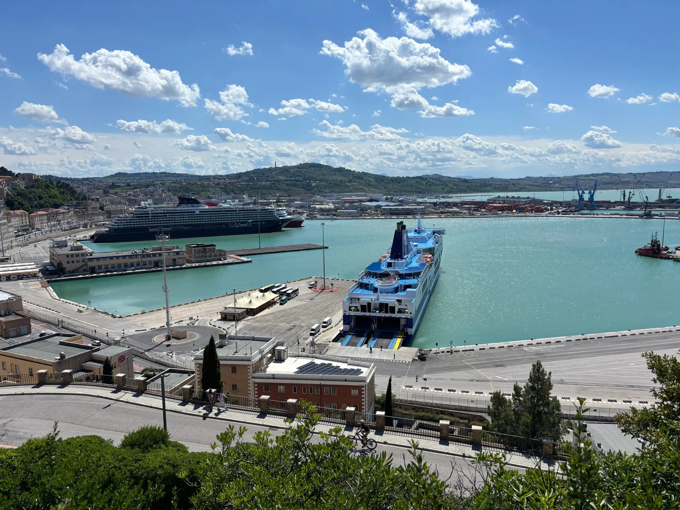 Explora I alongside the dock in a Mediterranean port, seen from the hill above the harbor